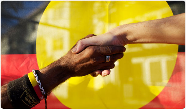 Indigenous and Non-Indigenous Australians shaking hands in front of the Aboriginal Flag. Photo: Gary Radler